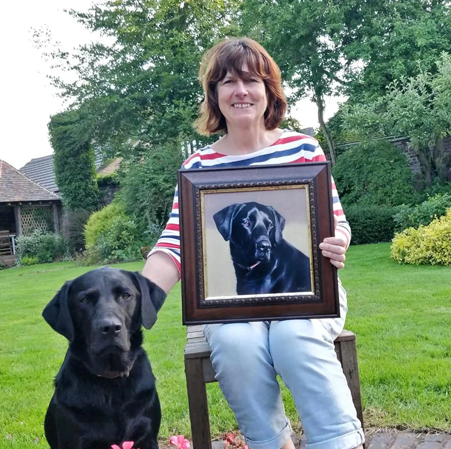 Mia the black Labrador with her framed birthday portrait and owner